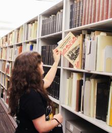 A picture of Amanda in the SCRC stacks, pulling a book from a shelf.